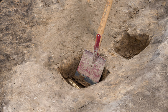 Shovel digging two small holes with buried pipes partially exposed